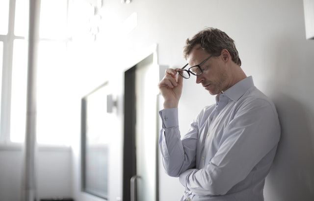 Man in glasses leaning against wall, exhausted