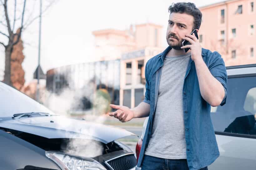 man on phone near broken-down vehicle