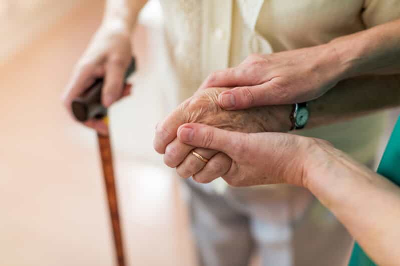 An elderly hand in held by a helper